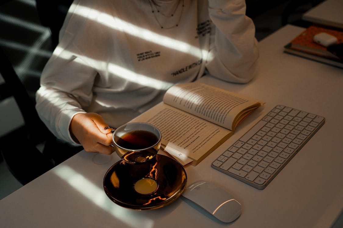free-photo-of-person-reading-a-book-and-drinking-tea-by-a-desk